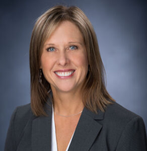 Angela Case is a professional woman with straight brown hair to her shoulders, she is wearing a grey blazer and smiling.