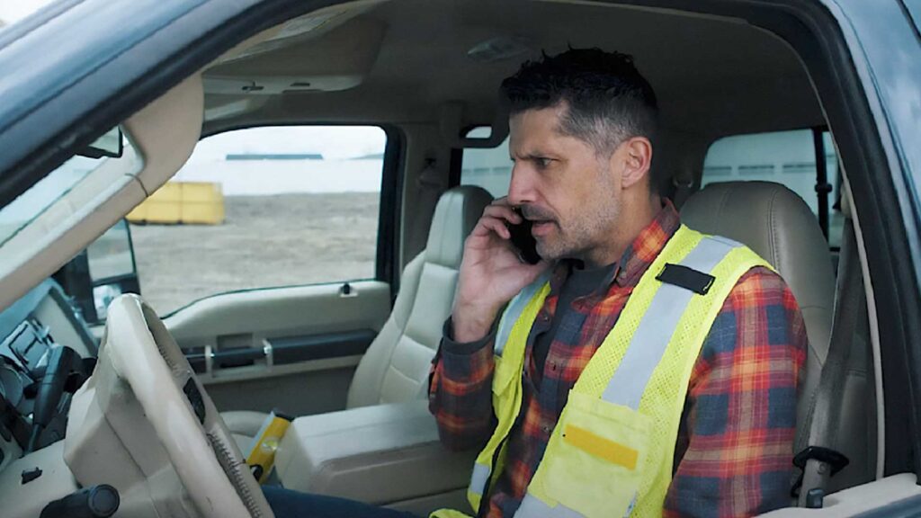 Man in a construction vest talking on the phone in his truck.