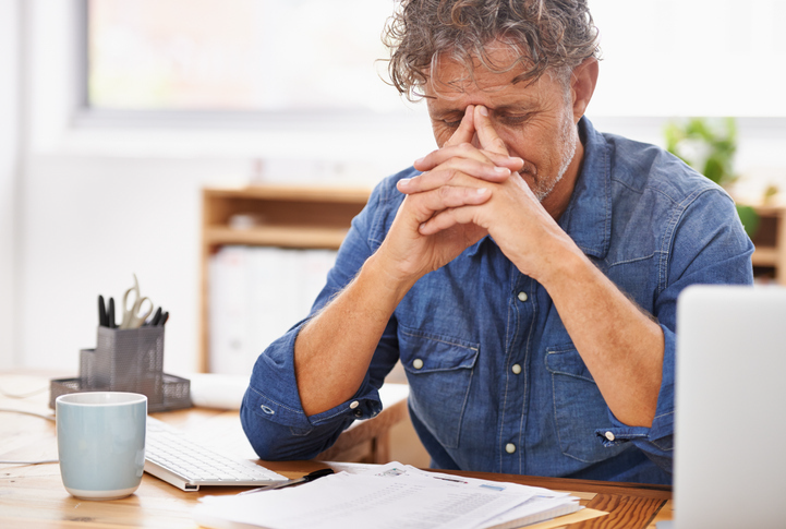 Revenue Officers - Older business man with his head in his hands at his desk looking stressed.